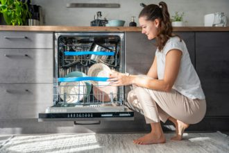 A woman putting dirty ceramic dish in the dishwasher. Household and helpful technology concept