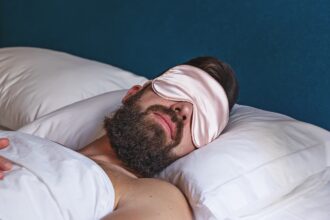 Closeup of bearded man in eye mask sleeping in bed. Concept of sleeping mask help by insomnia