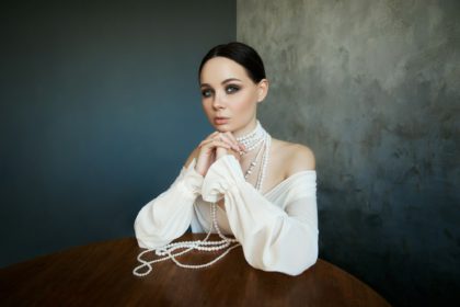 Girl dressed in white boho clothing with white pearl beads around her neck is sitting