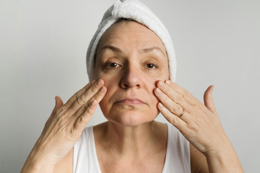 Middle-aged woman lookin in a mirror and checking bags under the eyes, skin and wrinkles. Skincare