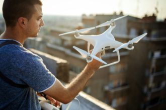 Young technician flying UAV drone with remote control on rooftop